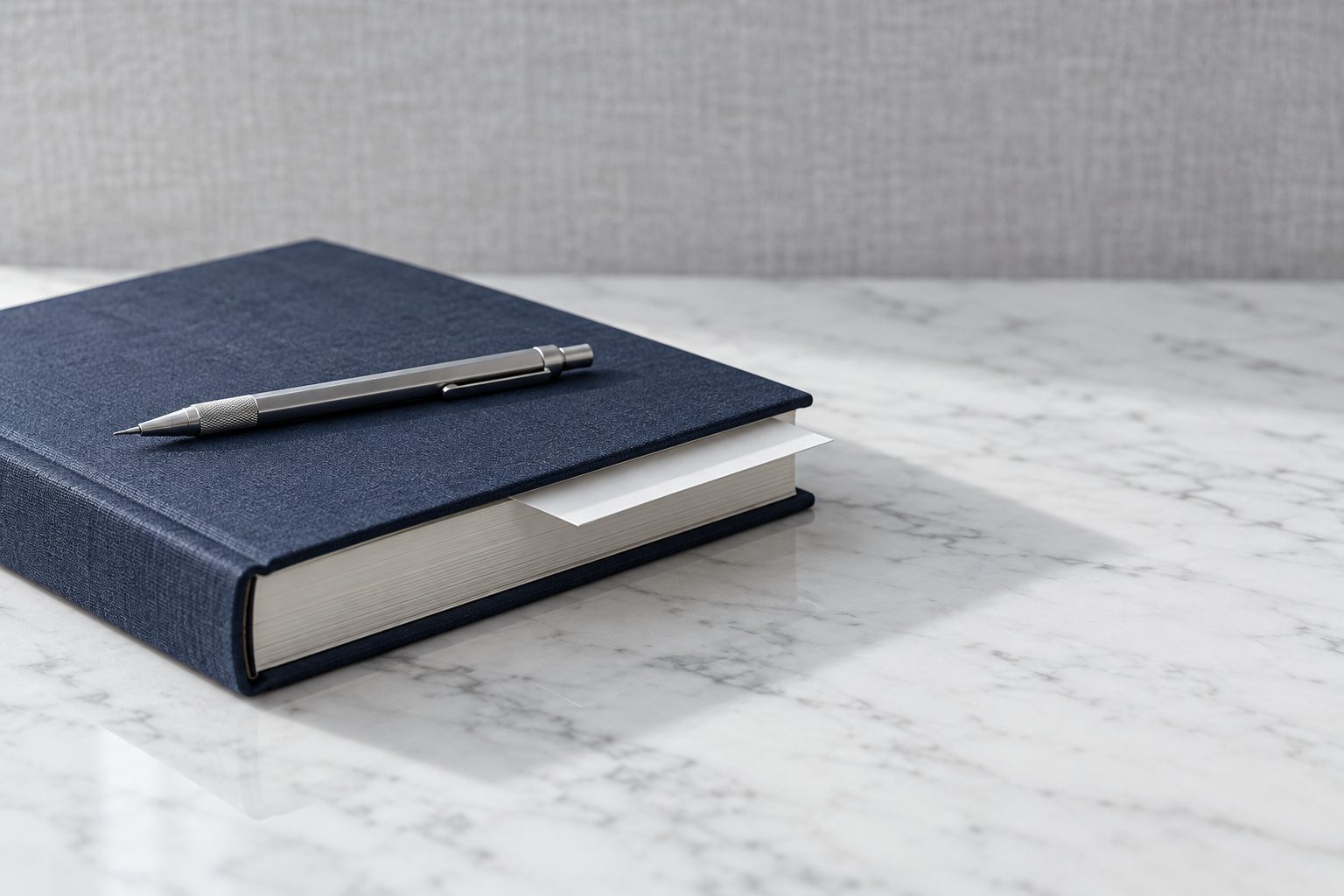 A navy cloth-bound ledger closed on a white marble surface with a silver pencil resting on it
