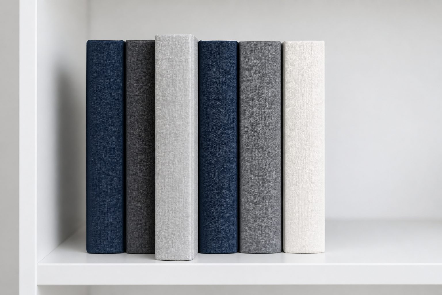 Six cloth-bound registers in navy, grey and off-white standing on a white shelf
